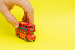 British toy double-decker red bus riding by male hand on yellow background. Concept of English language lesson and improving talking and speaking skills