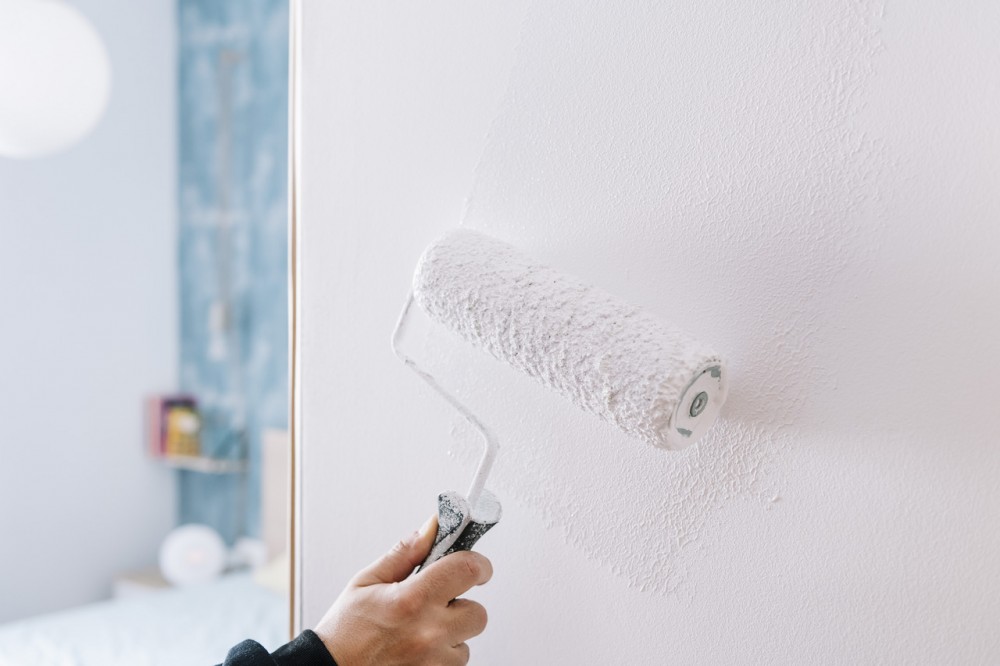 hand painting a wall in white with a roller, home decoration and renovation concept, horizontal photo with copy space for text