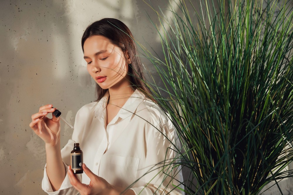 woman-hands-holding-massage-cosmetics-oil-bottle-applying-drops-skin-face-female-hold-oil-old-wall-background-with-shade-from-foliage-concept-healthy-lifestyle-self-care