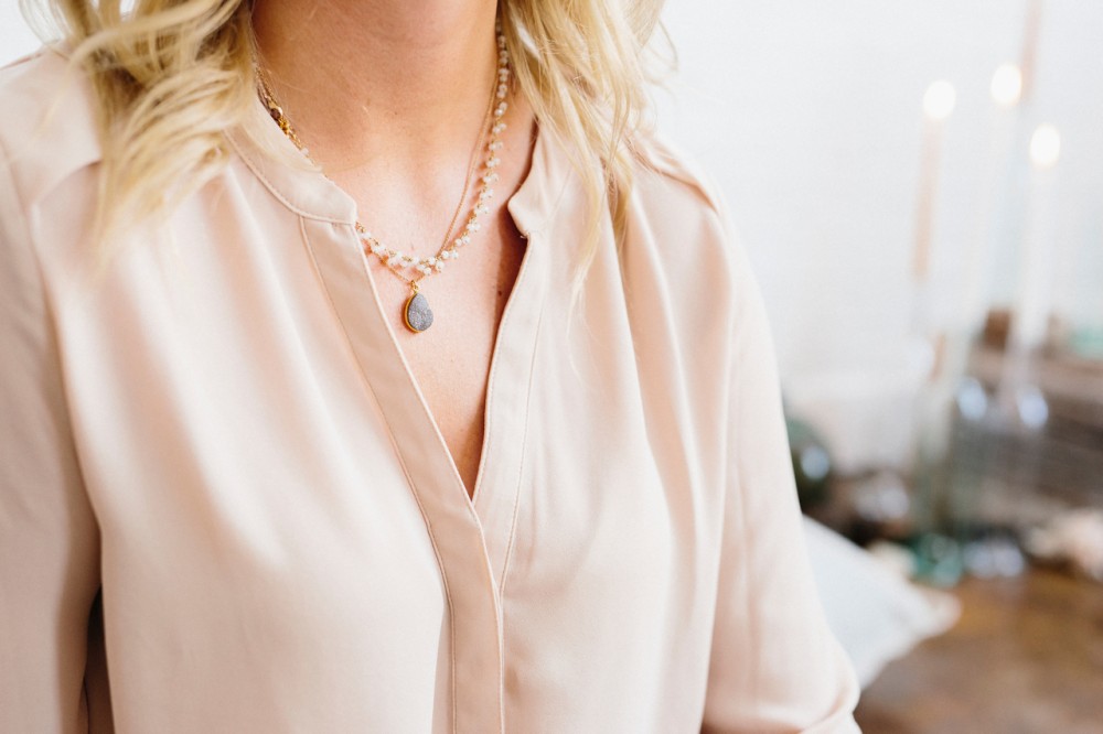 A woman in a silk shirt wearing a pendant necklace.